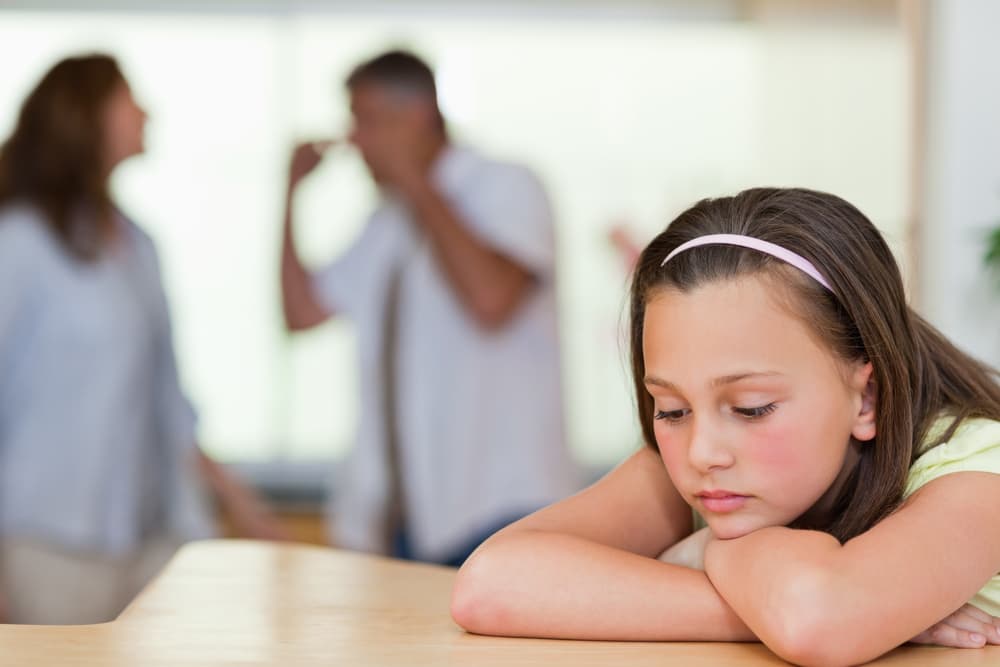 Sad looking girl with her fighting parents behind her