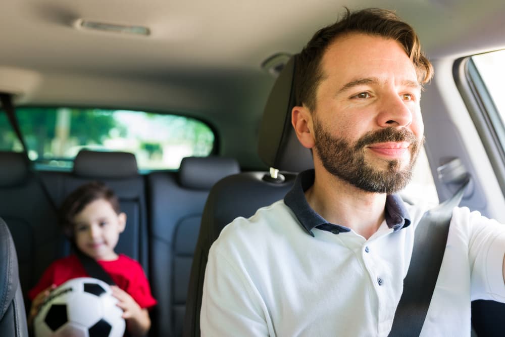 A father and son share a moment in the back seat of a car, navigating co-parenting through life's extracurricular activities.