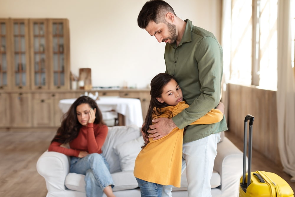 young girl hugging her father with mother sitting down in the background, child custody concept