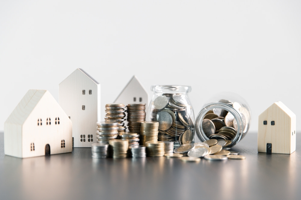 small replicas of homes with coins piled up in rental property concept image