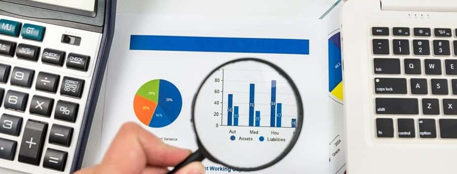 Close-up of a hand with a magnifying glass against the background of a chart. Compares statistical data, examines a business value in graphical charts, and analyzes trends, charts, and business patterns.