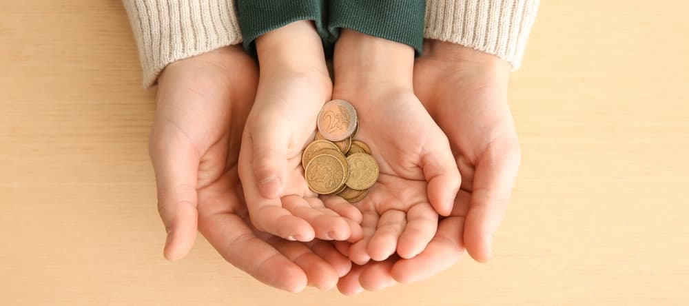 Hands of man and his son holding coins on wooden background. Concept of child support